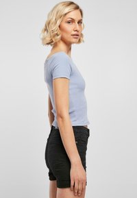 Top de culoare albastru deschis, cu dungi, cu mânecă scurtă, asortat cu pantaloni scurți negri cu mansete răsucite. Croiala este ajustată pe corp, evidențiind o siluetă elegantă.
