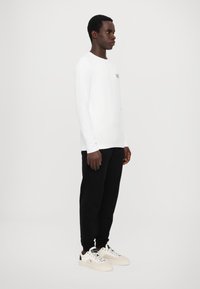 Hvit skjorte med lange ermer med en liten logo på venstre bryst, kombinert med svarte bukser og off-white joggesko. Enkel og minimalistisk design.