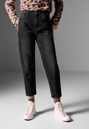 Sorte højtaljede jeans med lige ben, der har forlommer. Sammen med kremfarvede høje sneakers og stribede sokker.