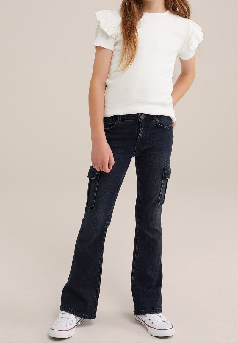 Vit ribbad kortärmad topp med volangdetaljer, matchad med mörkblå vida cargojoggers med sidofickor och vita sneakers.