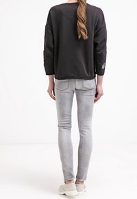 Felpa nera con maniche a tre quarti, abbinata a jeans grigi chiari aderenti e sneakers bianche. La felpa presenta un piccolo dettaglio ricamato.