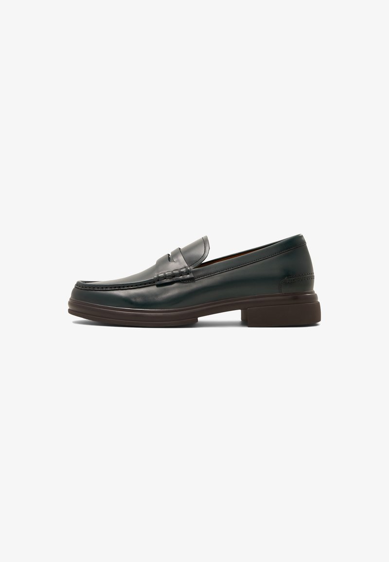Mocassin en cuir noir avec petit talon, surpiqûres, bande penny et semelle brun foncé, présenté de profil sur fond blanc.