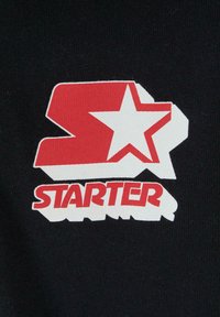 Juodas audinys su raudonu ir baltu spausdintu piešiniu, kuriame matosi raidės "S" ir "T" su žvaigžde ir žodžiu "STARTER" žemiau.