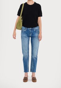 Haut noir en maille côtelée à manches courtes, jean bleu clair à jambes droites, chaussures marron à enfiler avec des accents gris. Sac à épaule vert olive.