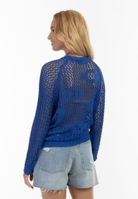 Blå strikket sweater med åben netdesign og blomster mønster, parret med lyse denimshorts med flossede kanter.