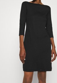 Robe noire à manches trois-quarts avec un col bateau, forme ajustée et texture douce, avec un ourlet simple et sans motifs supplémentaires.