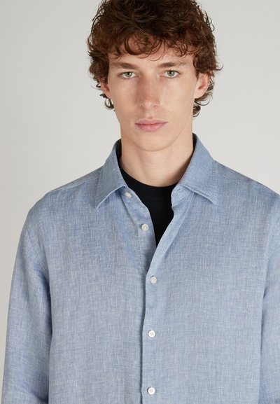 Camisa de lino azul claro con cuello de botón, tejido texturizado y botones blancos. Mangas largas y un corte relajado.