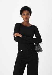 Zwarte ribbel longsleeve met een ronde hals, gecombineerd met hoge zwarte jeans en een kleine zwarte handtas.