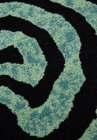Sort og teal tæppe med et spiral mønster. Den strukturerede, bløde overflade har en blanding af mørke og lyse grønne nuancer i et bølget design.