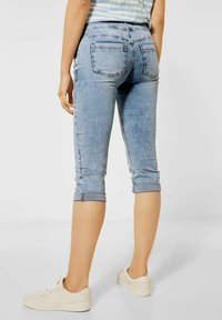 Pantaloni capri in denim azzurro chiaro con orli arrotolati, dotati di tasche posteriori e design aderente, abbinati a scarpe da ginnastica bianche.