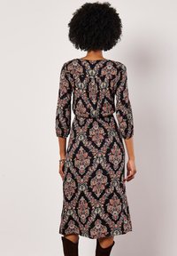 Czarna sukienka w kwiatowy wzór paisley w odcieniach czerwieni, zieleni i kremu. Rękawy do trzech ćwiartek oraz dopasowana talia, sięgająca tuż poniżej kolana.