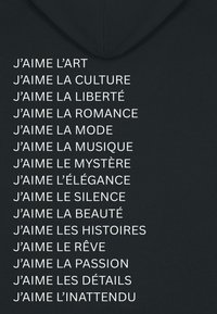 Black hoodie featuring white text arranged in vertical columns, listing various phrases starting with "J'aime." Simple, clean typography.
