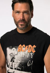 Svart ärmlös T-shirt med ett grafiskt tryck av AC/DC med ordet "FIFTY" i orange. Tillverkad av mjuk bomull, med en klassisk rundad halsringning.