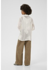 Lightweight, sheer white blouse with floral embroidery, paired with wide-leg brown corduroy pants and black and white striped shoes.