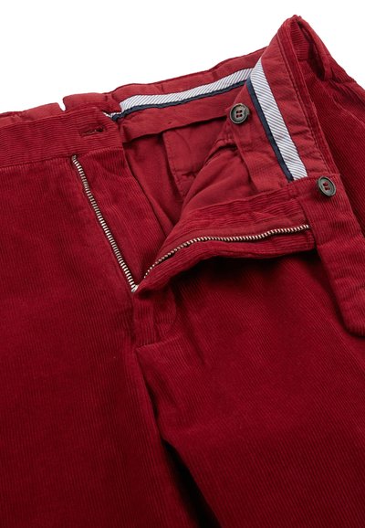 Pantalones de pana rojos con cierre de cremallera y botón. Presentan un interior de cinturilla a rayas y una textura de canalé horizontal.