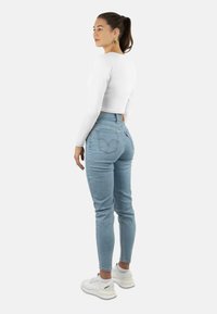 Hellblaue High-Waist-Jeans mit schmalem Bein, kombiniert mit einem weißen, kurz geschnittenen Langarmshirt. Weiße Sneakers runden das Outfit ab.