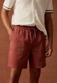 Rode katoenen shorts met een elastische tailleband en trekkoorddetails. Zijzakken en een rechte snit. Gemaakt met een textuur crème shirt.