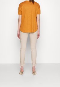 Hořčicově žluté tričko s krátkým rukávem, volný střih, zkombinované se světlými béžovými slim kalhotami a béžovými sandály na podpatku. Jednoduchý, ležérní outfit.