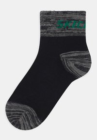 Mustvalge sokk halli mustriga kraega, tugevdatud kontsaga ja rohelise brändi logoga. Materjal näeb välja pehme ja tekstuurne.