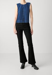 Haut en denim sans manches avec un col rond, associé à un jean flare noir ajusté et des bottines à talons noires.