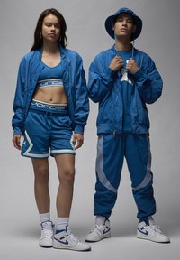 Ropa deportiva azul que incluye una chaqueta bomber, un top corto, pantalones cortos y pantalones de chándal, con acentos blancos contrastantes y zapatillas deportivas.