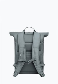 Sac à dos gris à rabat, équipé d'un dos en maille rembourrée, de bretelles ajustables, d'une poignée extérieure, et d'un design minimaliste avec une texture de tissu robuste.