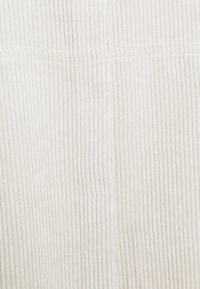 Close-up of white corduroy fabric showing vertical ridged texture and a horizontal seam across the middle.