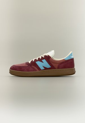 Baskets New Balance marron et brun avec logo "N" bleu ciel et languette de talon, lacets beige et semelle couleur gomme sur fond neutre.