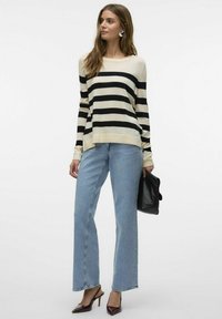 Maglione a righe in crema e nero, vestibilità rilassata; abbinato a jeans a vita alta blu chiaro, pochette nera e décolleté a punta.