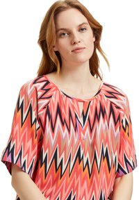 Haut en tissu léger avec un motif zigzag multicolore. Il dispose de manches courtes, d'un col rond et d'une ouverture en forme de clé à l'avant.