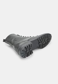 Stivale alla caviglia in pelle nera con parte superiore texture e suola in gomma robusta. Presenta una linguetta e cuciture decorative lungo i lati.