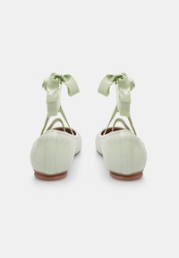 Gaišzaļi ādas baleta zābaki ar noapaļotu pirkstu daļu, ar krustenisku siksniņu dizainu un lentēm aizmugurē, demonstrējot gludu tekstūru.