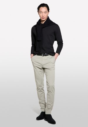 Maglietta nera a maniche lunghe, pantaloni grigio chiaro, cintura nera. Sciarpa nera drappeggiata sulle spalle, stivali neri alla caviglia. Texture morbide e aderenti.
