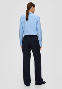 Helles blaues Langarmhemd mit Button-Down-Kragen, kombiniert mit dunkelblauen, weit geschnittenen Hosen mit Gesäßtaschen. Überall glatte Textur.