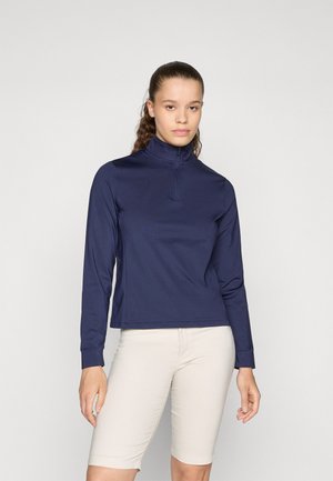 Mornarska bluza dugih rukava s polu-zip ovratnikom, glatka tkanina i opušteni kroj, uparen s svijetlim bež šortsevima.