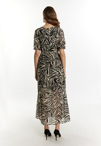 Maxikleid mit einem schwarz-beigen abstrakten Zebra-Muster, kurzen puffärmel, tailliertem Schnitt und einem fließenden, halbtransparenten Stoff.