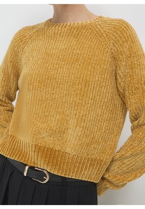 Pull en maille côtelée jaune doré porté avec un pantalon noir et une ceinture noire avec une boucle argentée.