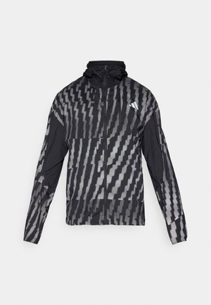 Veste noire légère avec un motif géométrique blanc. Comprend un col haut, une fermeture éclair sur le devant et des manches longues.