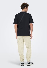 T-shirt en coton noir, coupe décontractée, associé à un pantalon cargo beige clair avec des poches latérales, et des baskets noires et blanches.