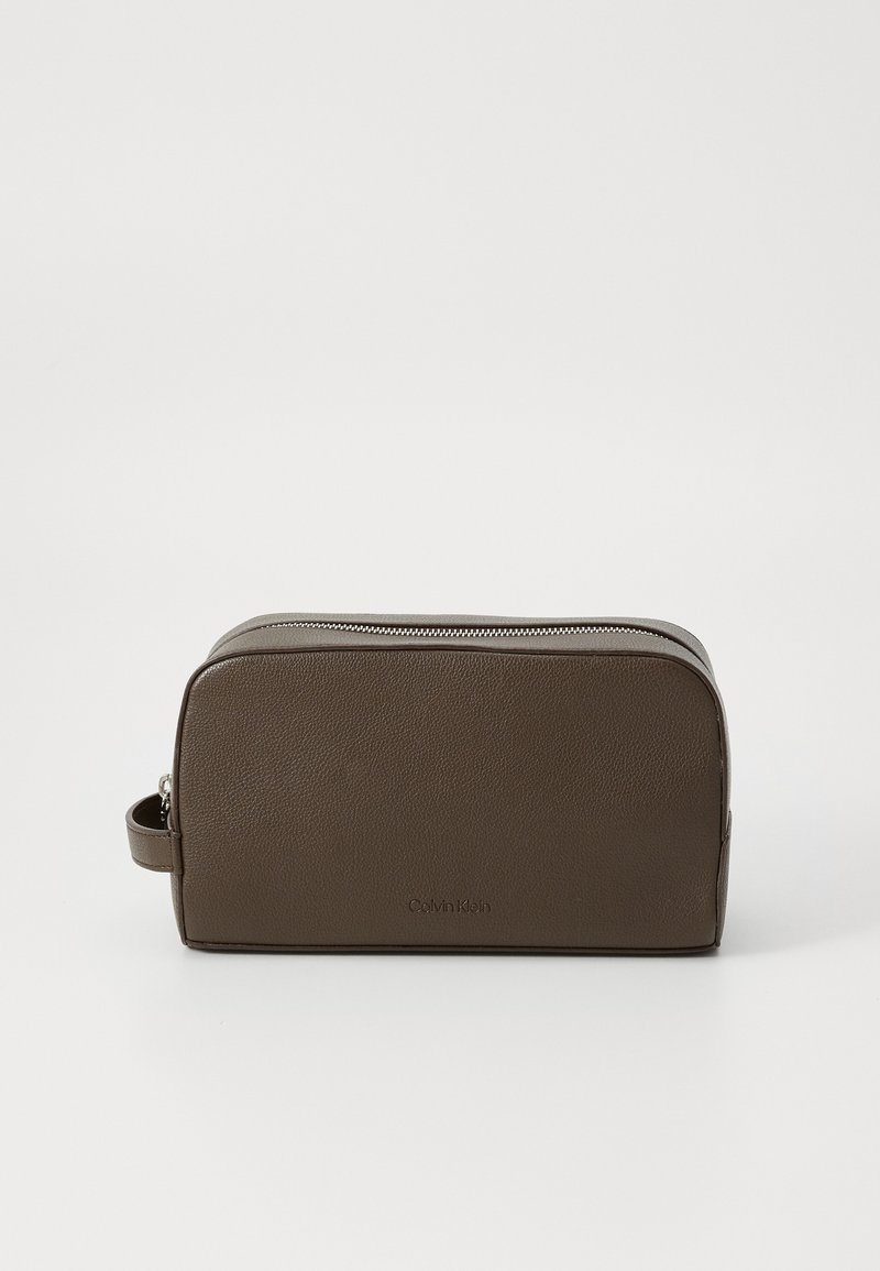 Trousse de maquillage en faux cuir marron avec une forme arrondie, fermeture éclair sur le dessus et poignée latérale ; présente un logo en relief à l'avant.