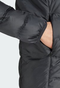 Svart puffjacka i detalj som visar en närbild av en vadderad ärm och en öppen dragkedjeficka, vilket framhäver dess material och textur.