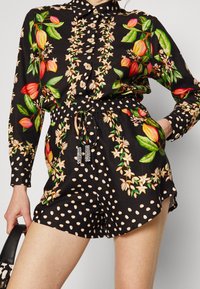Vestido tipo camisa con estampado floral, base negra con flores multicolores y pantalones cortos de lunares, cintura ajustada, cierre de botones, cuerda elástica.