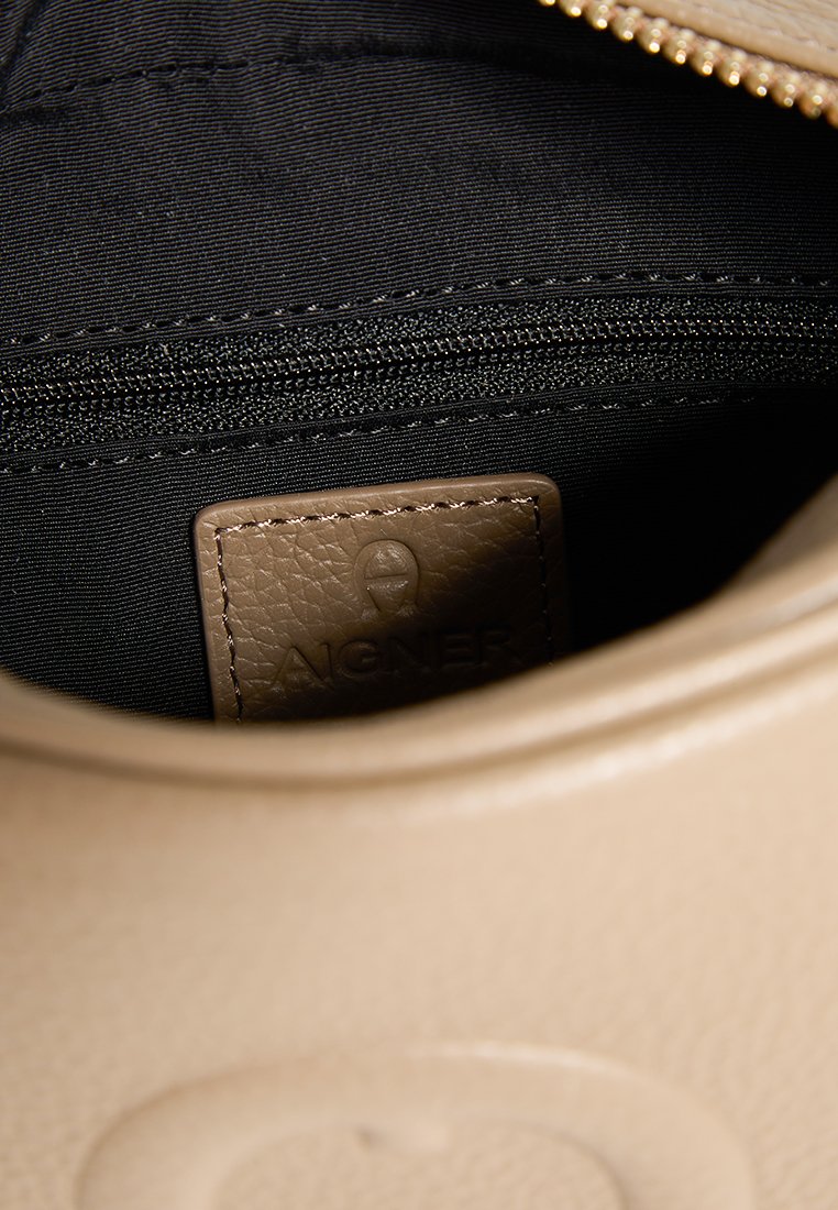 Beige Lederhandtasche mit einem Innenfach, das eine Reißverschlusstasche und ein schwarzes Futter enthält. Enthält ein sichtbar geprägtes Etikett mit der Aufschrift "AIGNER."