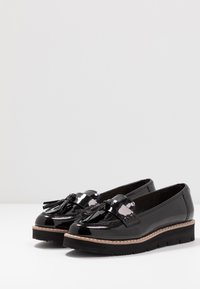 Sorte patenterte lær loafers med flat plattformsåle, med frynse detaljer og sydd dekorasjon langs kanten.