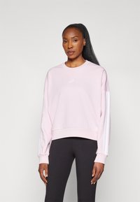 Rosa genser med rund hals, ribbestrikket kant og hvite tre-stripes aksenter på ermene. Mykt, teksturert materiale med en avslappet passform.