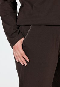 Maglietta marrone a maniche lunghe realizzata in morbido tessuto, abbinata a pantaloni marroni con tasche laterali e un design slim fit, con dettagli di cucitura discreti.