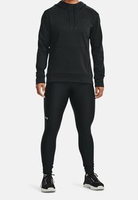 Czarna bluza z kapturem z kieszenią z przodu i czarne legginsy. Oba wykonane z gładkiego materiału, noszone z czarnymi sneakersami.