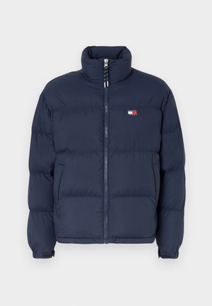 Granatowa kurtka puchowa z wysokim kołnierzem, zamek błyskawiczny i poziomy wzór pikowania. Posiada małą naszywkę z logo w kolorze czerwonym, białym i niebieskim.