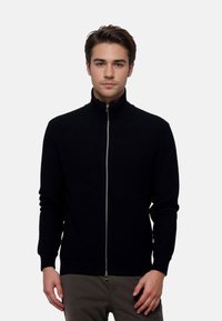 Black ribbed zip-up sweater with a high collar, fitted sleeves, and a smooth zipper; made from soft, textured material.