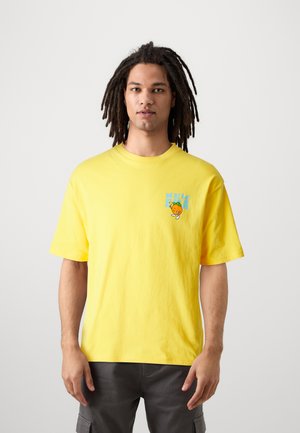 Camiseta de algodón amarilla con mangas cortas, que presenta un texto gráfico azul y un personaje naranja en el área del pecho izquierdo. Diseño simple.